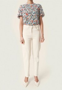 Blommönstrad kortärmad topp i grått med röda, blå och beige mönster; tillsammans med krämfärgade skräddarsydda byxor och vita spetsiga klackar.