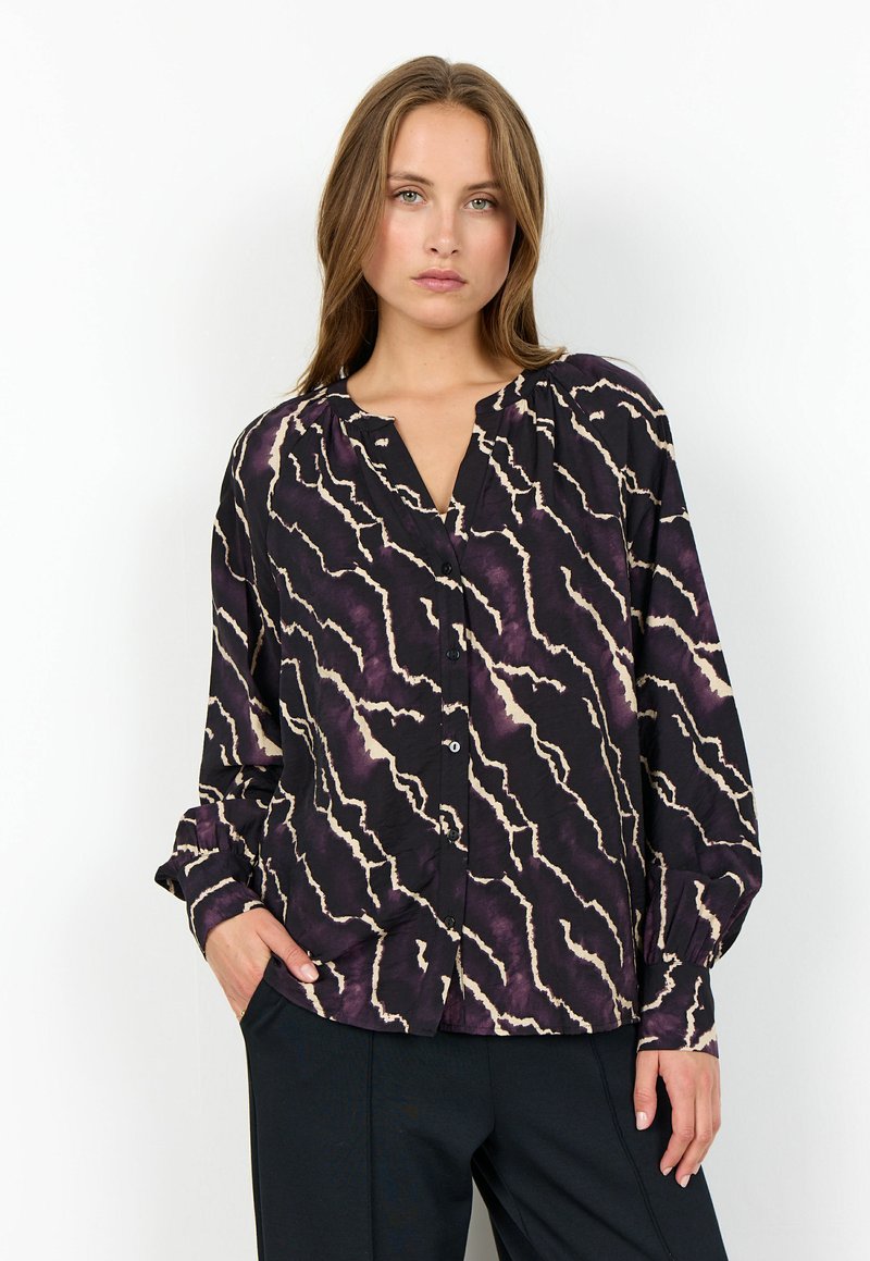 Svart blus med ett vågigt lila och krämfärgat mönster, knappar fram, v-ringning och långa ärmar. Tillverkad av ett lätt, texturerat tyg.
