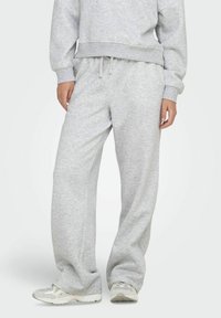 Grijze sweatpants van zacht materiaal, met een tailleband met trekkoord, ruime pijpen en subtiele textuur, gecombineerd met lichte sneakers.