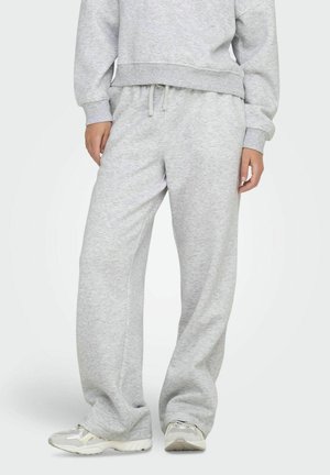 Pantaloni grigi in felpa realizzati in tessuto morbido, con vita regolabile da un cordino, gambe larghe e una trama sottile, abbinati a sneakers chiare.