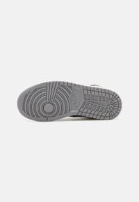 Podeszwa sneakersów Nike, głównie w odcieniach szarości, ma okrągłe i poziome wzory bieżnika, z nadrukowanym logo z boku oraz teksturowaną powierzchnią dla lepszej przyczepności.
