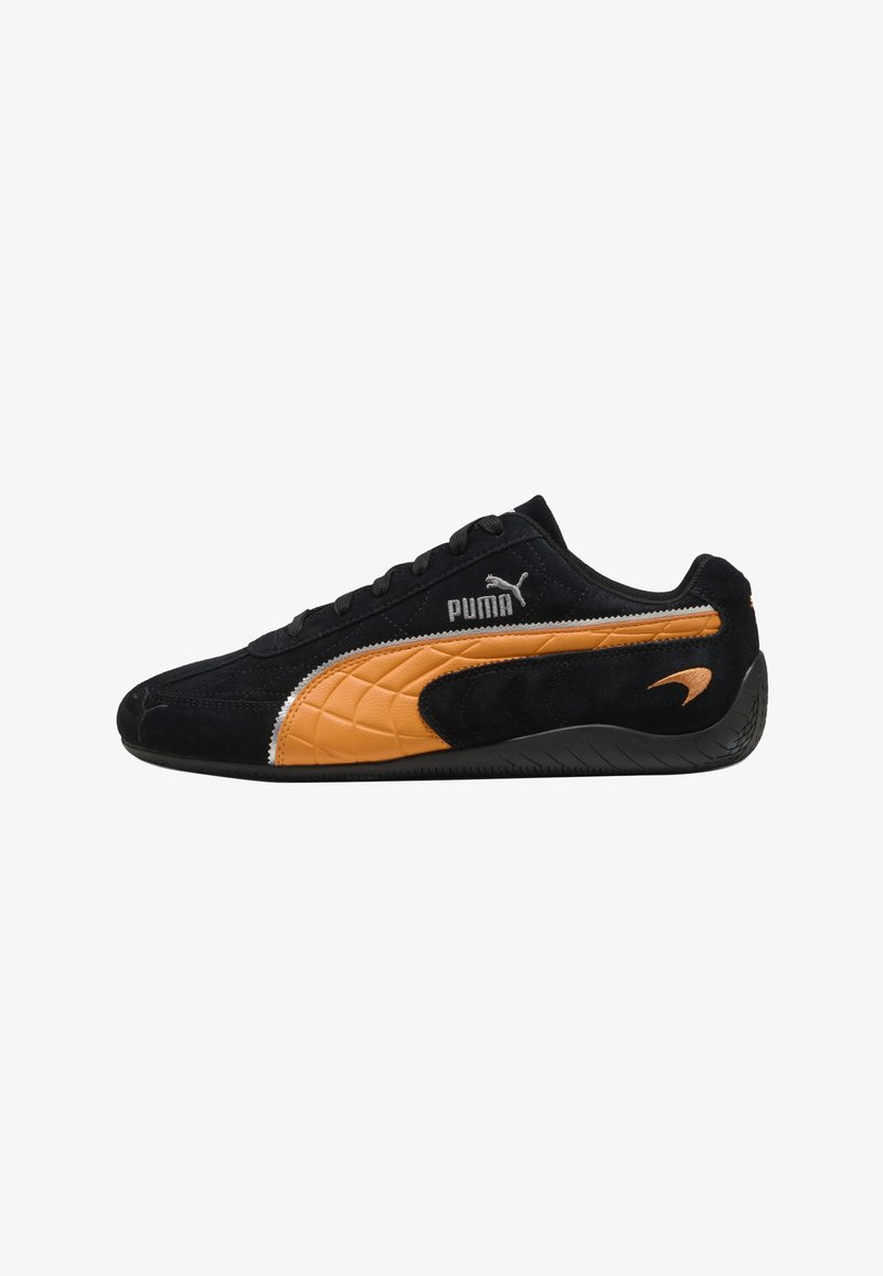 Baskets Puma basses noires avec bande latérale orange, semelle noire et logo Puma près des lacets et du talon.