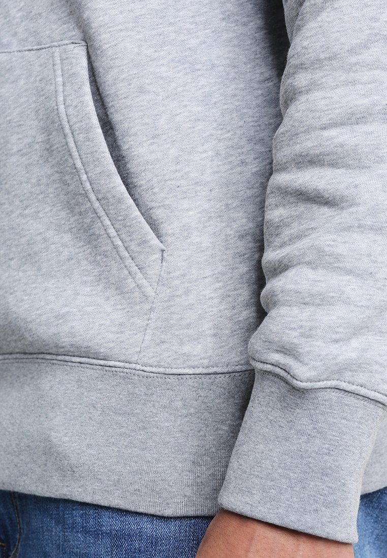 Felpa grigia in cotone con tasca a marsupio, polsini a coste e una tessitura morbida. I dettagli delle cuciture a vista arricchiscono il design complessivo.