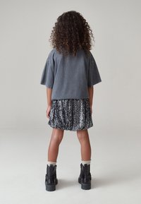 Maglia grigia oversize a maniche corte, gonna nera con paillettes e stivaletti neri con suola spessa, vista da dietro.