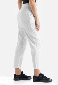Valkoiset korkeavyötäröiset housut, joissa on slim fit -leikkaus, sivutaskut ja sileä pinta. Yhdistetty mustiin lenkkikenkiin.