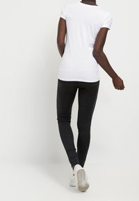 Camiseta blanca de manga corta combinada con jeans ajustados negros. El conjunto se completa con zapatillas blancas, mostrando un estilo informal.