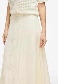 Longue jupe ivoire fluide en tissu texturé avec une apparence légèrement plissée. Taille mi-haute, légère et respirante.