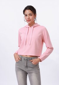 Felpa rosa corta con un motivo a zigzag testurizzato, dotata di tasca frontale e cappuccio con cordino. Abbinata a jeans grigi chiari a vita alta.