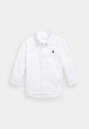 Chemise blanche à manches longues pour enfants avec col boutonné et petit logo brodé bleu marine sur la poitrine.