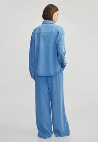 Outfit in denim blu chiaro caratterizzato da una camicia a taglio rilassato con ricami sottili e pantaloni a gamba larga, che presentano una consistenza liscia e un design informale.