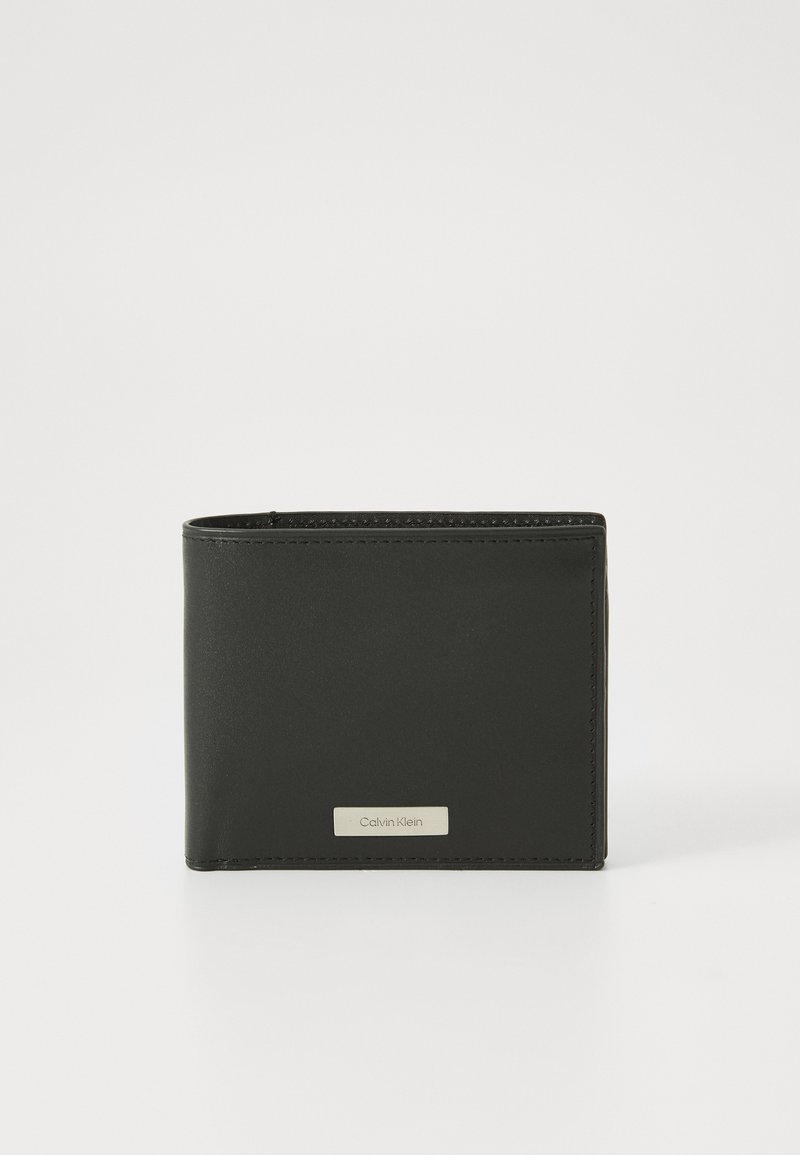 Portefeuille en cuir noir avec une texture lisse, de forme rectangulaire et des bords surpiqués. Présente une plaque de logo argentée sur le devant.