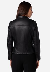Giacca in pelle nera con design aderente, texture liscia e cuciture visibili. Caratterizzata da polsini con zip e colletto alla coreana.
