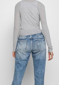 Grå långärmad topp i kombination med urtvättade blå denimjeans som har två bakfickor och en avslappnad passform. Slät textur på tygytorna.