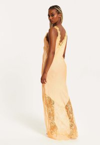 Peach-colored dress with lace accents, featuring adjustable straps and a flowing silhouette, partially lined with intricate lace at the hem.