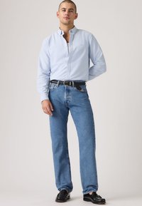 Ανοιχτό μπλε πουκάμισο με κουμπιά, εφαρμοστά τζιν, μαύρη πλεκτή ζώνη και μαύρα παπούτσια. Καθαρές γραμμές, κλασικός σχεδιασμός, casual αισθητική.