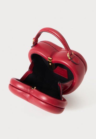 Petit sac à main en cuir rouge avec fermoir doré, ouvert pour montrer l’intérieur noir et une poignée unique sur le dessus, sur un fond clair uni.