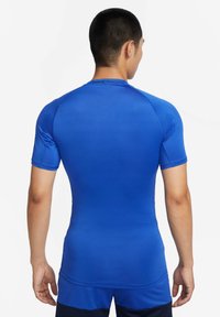 Blå atletisk kompresjonsskjorte med korte ermer, glatt tekstur og tettsittende design. Har "NIKE PRO" merke nær kragen.