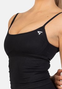 Czarny sportowy top na ramiączkach z cienkimi paskami, charakteryzujący się dopasowanym krojem, teksturowanym wzorem po bokach oraz małym białym logo na piersi.