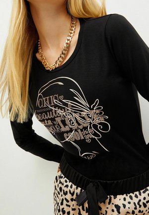 Haut à manches longues noir avec une coupe décontractée, arborant un motif graphique métallique doré. Texture lisse avec un col rond et un ourlet arrondi.