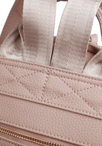 Jasnoróżowa torebka wykonana z teksturowanej ekoskóry z diagonalnymi przeszyciami i beżowymi materiałowymi ramiączkami. Posiada metalowy zamek błyskawiczny.