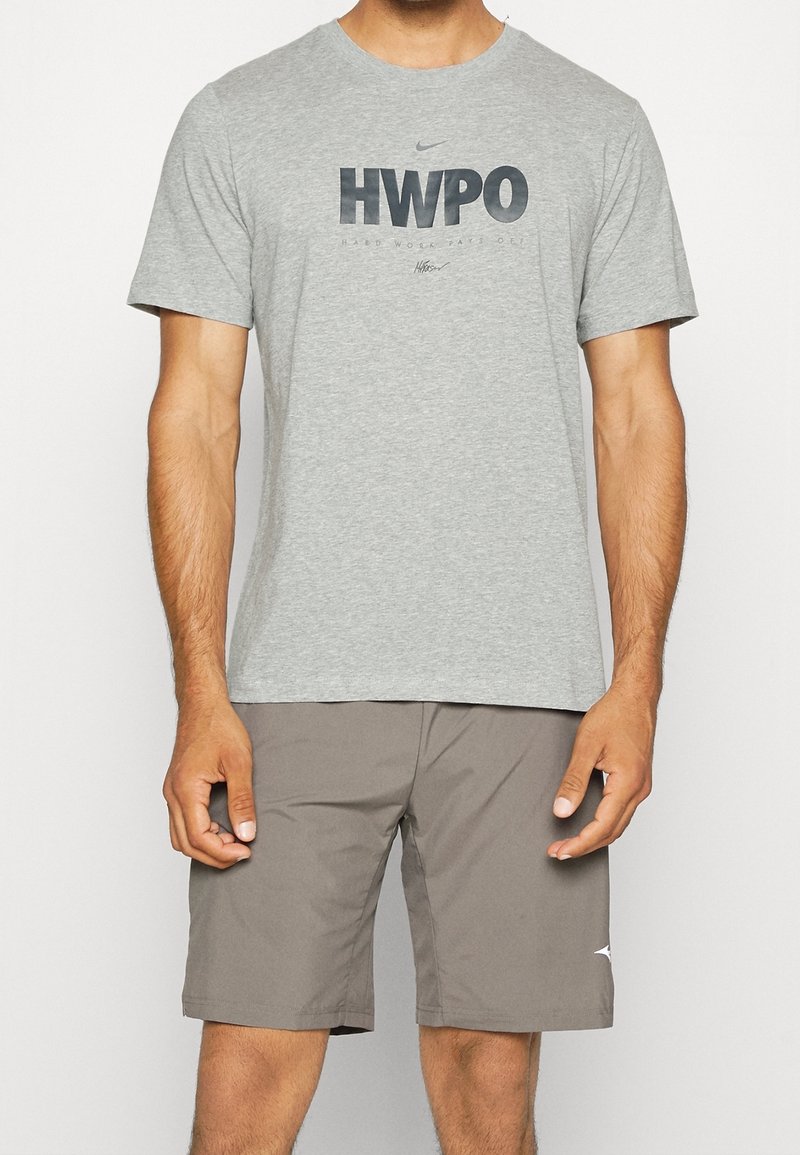Camiseta de algodón gris con gráfico "HWPO" en azul oscuro, combinada con pantalones cortos de color marrón claro. La camiseta tiene mangas cortas y un escote redondo.