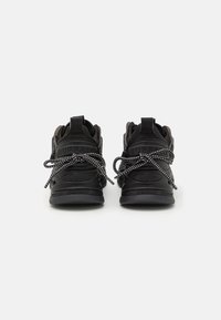 Svart sneakers med teksturert overdel, kraftige snøringer og polstret krage. Har en logo bak og en tykk gummisåle for støtte.