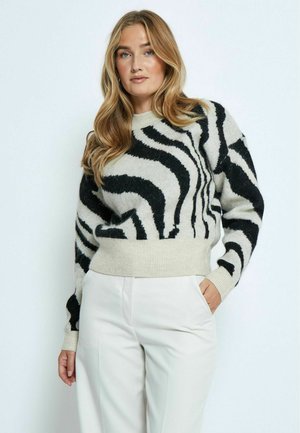 Maglione a strisce zebrate in bianco e nero realizzato in morbido tessuto a maglia, con orlo e polsini a coste, indossato con pantaloni di colore chiaro.