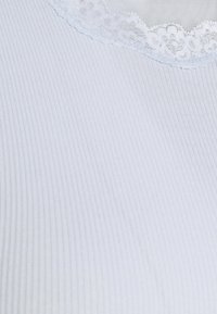 Světlé modré žebrované látky s krajkovým lemem na výstřihu. Textura je měkká a mírně elastická s jemným květinovým vzorem v krajce.