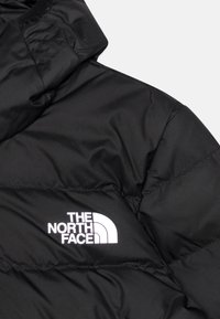 Sort isoleret jakke med et quiltet design og et fremtrædende hvidt logo fra The North Face på venstre brystområde.