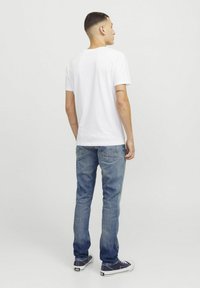 T-shirt en coton blanc avec un col rond, associé à un jean en denim bleu. Le jean comprend des poches arrière et un léger délavage. Des baskets noires complètent le look.