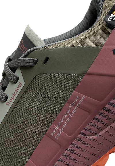 Gros plan sur une chaussure de sport verte et marron avec un tissu texturé, des lacets, et le texte "Tropicfeel" et "Performance par Nature Conçu pour l'Exploration."