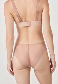 Completo di reggiseno e mutande nude senza cuciture realizzato in un tessuto liscio e elastico, con spalline regolabili e un design minimalista, privo di cuciture visibili.