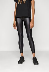 Schwarze, glänzende Leggings aus dehnbarem Material, eng anliegend, kombiniert mit einem schwarzen T-Shirt mit kurzen Ärmeln und Leopardenmuster.