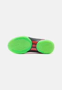Sort sportsko sål med grøn gummioverflade, der har spiral mønstre og røde accenter. Glat tekstur og kurvet design.