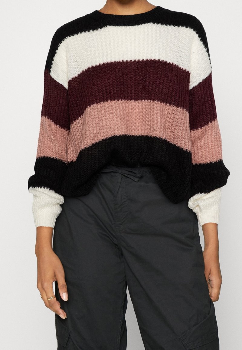 Pull-over en tricot avec de larges rayures noires, blanches, bordeaux, roses et noires. Caractéristiques : coupe ample et poignets côtelés.