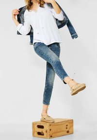 Vit, texturerad blus med dragsko, tillsammans med ljusblå skinny jeans och beige espadriller, stående på en träkista.