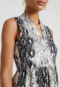 Czarna i biała sukienka bez rękawów z dekoltem w serek, ozdobiona teksturowanym wzorem wężowej skóry. Materiał jest lekki i zwiewny, z marszczeniem w talii.