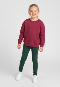 Bordowa bluza z długimi rękawami i okrągłym dekoltem, zestawiona z zielonymi legginsami i białymi trampkami. Prosty i dopasowany krój.