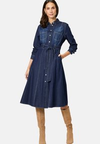 Denim shirtjurk met lange mouwen, twee borstzakken, een ceintuur op de taille en contrasterende stiksels. Verkrijgbaar in donkerblauwe denim.
