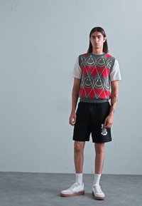 Grå strikket genser med rød og gul mønster, hvit t-skjorte, sorte shorts og hvite joggesko med lysebrune såler. Enkelt, moderne design.