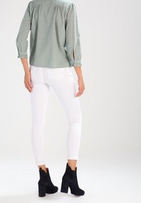 Light green blouse with gathered details, white fitted jeans, and black suede ankle boots with block heels and cut-out accents.