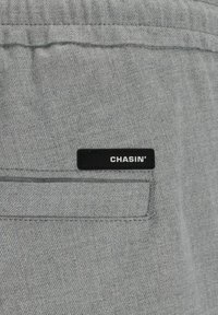 Poche en tissu gris avec une étiquette rectangulaire noire affichant "CHASIN'" en lettres majuscules blanches.
