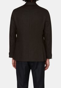 Blazer marrone su misura con una silhouette strutturata, spacco singolo e polsini con bottone. Realizzato in tessuto strutturato, abbinato a pantaloni scuri.