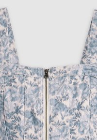 Top de denim floral com alças finas, padrão azul claro e branco, apresentando um zíper central e costuras estruturadas para ajuste e forma.