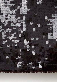 Primer plano de brillantes lentejuelas circulares negras y plateadas superpuestas que crean una superficie texturizada y reflectante de tela.