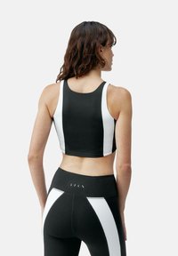 Crop top athlétique noir et blanc avec un col rond et un design dos nageur ; texture lisse et silhouette ajustée.