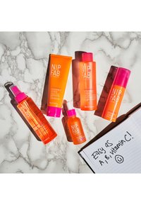Pięć produktów do pielęgnacji skóry NIP+FAB w pomarańczowych plastikowych butelkach z różowymi nakrętkami. Zawiera peeling, tonik, serum i mgiełkę. Marmurowe tło.