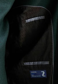 Interior de una chaqueta de tela verde con un forro negro de diseño, que presenta una etiqueta "ZIGNONE ACTIVE" y dos bolsillos con ribete gris.