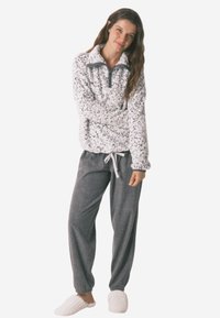 Fleecepullover med høj krave og leopardprint, parret med mørkegrå sweatpants og cremegarnslippers. Blød tekstur generelt.