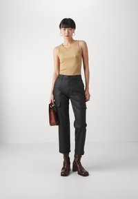 Brun ribbet tank topp, svarte cargo bukser med lommer, og burgunder ankelstøvler. Tilbehør inkluderer en brun håndveske og hoop-øredobber.